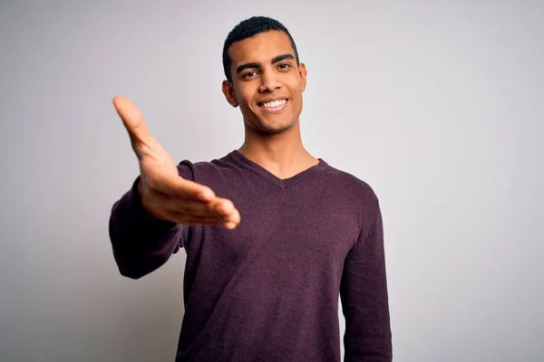 白い背景にカジュアルなセーターを着た若いハンサムなアフリカ系アメリカ人男性が挨拶や歓迎として握手を提供する優しい笑顔 成功事業 — ストック写真