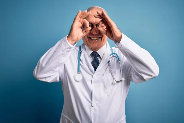 Starszy Siwowłosy Lekarz Noszący Stetoskop Płaszcz Medyczny Niebieskim Tle Wykonujący — Zdjęcie stockowe