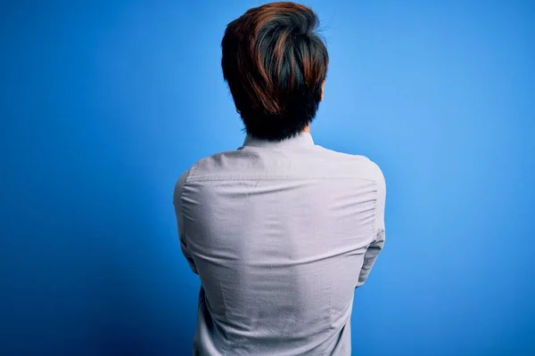 Young handsome chinese man wearing casual shirt standing over isolated blue background standing backwards looking away with crossed arms
