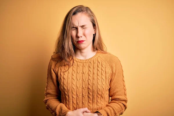 年轻美丽的金发女人穿着宽松的毛衣站在黄色的背景上 双手放在肚子上 因为消化不良 痛苦不堪 阿切概念 — 图库照片