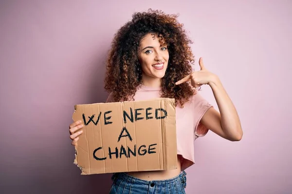 Young beautiful activist woman with curly hair and piercing protesting asking for a change with surprise face pointing finger to himself