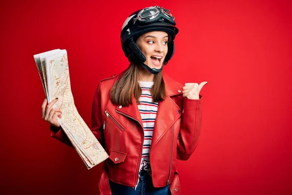 若い美しい観光客のオートバイのヘルメットをかぶって女性都市地図を保持し 幸せな顔の笑顔で親指で側まで示す — ストック写真