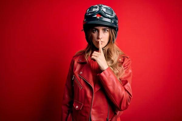 若い美しいブルネットのオートバイの女性は唇に指で静かになるように求めている赤い背景の上に元ヘルメットを着ています 沈黙と秘密の概念 — ストック写真