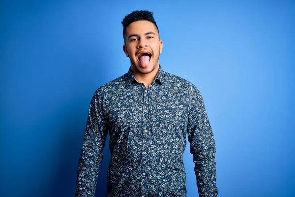 孤立した青い背景の上に立ったカジュアルなシャツを着た若いハンサムな男が面白い表情で幸せ舌を突き出している 感情概念 — ストック写真