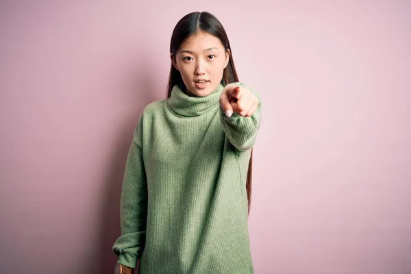 若いです美しいですアジアの女性身に着けています緑冬セーター上のピンクSolated背景を指して不満とフラストレーションへカメラ 怒っていると激怒とともにあなた — ストック写真