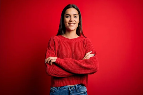 Beautiful young brunette woman wearing casual sweater standing over red isolated background smiling with happy face winking at the camera doing victory sign. Number two.