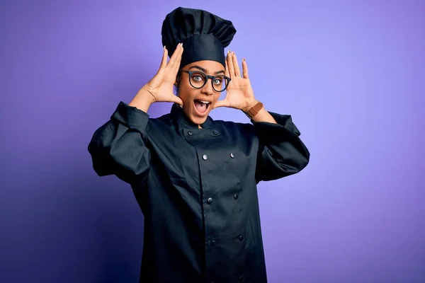 Young african american chef girl wearing cooker uniform and hat over purple background Smiling cheerful playing peek a boo with hands showing face. Surprised and exited