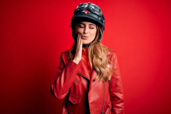 歯の痛みや歯の病気のために痛みを伴う式で手で口に触れる赤い背景の上に元ヘルメットを身に着けている若い美しいブルネットのオートバイの女性 歯医者 — ストック写真