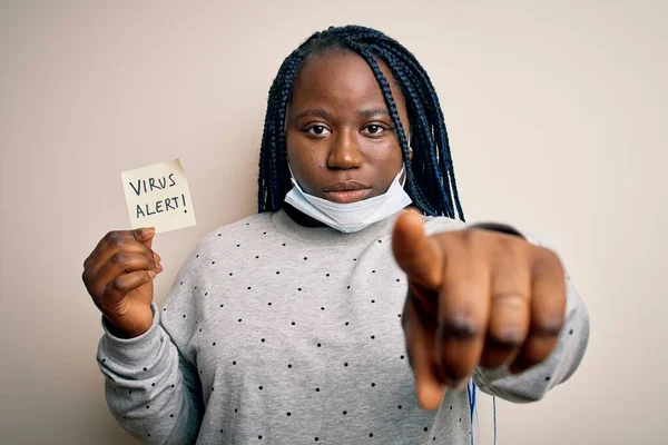 African american woman wearing medical mask holding reminder with virus alert message pointing with finger to the camera and to you, hand sign, positive and confident gesture from the front