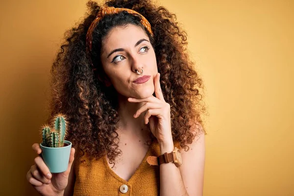 質問について考えるサボテンの植物の深刻な顔を持つ巻き毛とピアス保持ポットを持つ若い美しい女性は 非常に混乱したアイデア — ストック写真