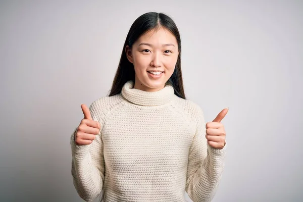 孤立した背景成功サインの上に立つカジュアルなセーターを着て若い美しいアジアの女性は 手で積極的なジェスチャーを行うと 親指を笑顔と幸せ 陽気な表情と勝者のジェスチャー — ストック写真