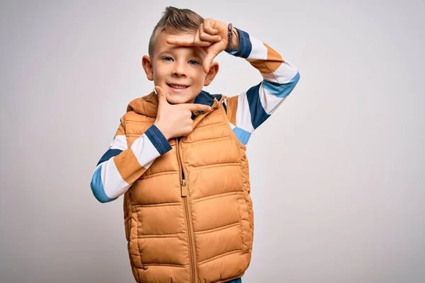 青い目の若い白人の子供は 手と幸せな顔をした指でフレームを作る孤立した背景笑顔の上に冬のコートを着て立っています 創造性と写真の概念 — ストック写真
