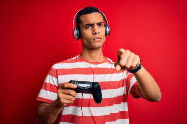 Yakışıklı afro-amerikan oyuncu video oyunu oynuyor jostick ve kulaklıkla kamerayı işaret ediyor ve sen, el işareti, ön taraftan pozitif ve kendinden emin bir jest.