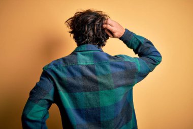 Sarı arka planda duran, gündelik tişört giyen genç yakışıklı adam, elleri kafasında şüpheyi düşünerek geriye doğru gidiyor.