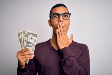 Yakışıklı Afro-Amerikalı adam elinde bir deste banknotla beyaz arka planda kapak ağzı utançla kaplanmış, korku ifadesi, sessizlikten korkmak, gizli bir konsept.