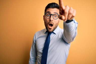 Sarı arka planda duran kravat ve gözlük takan genç yakışıklı işadamı. Parmağıyla işaret ediyor. İleriye şaşırmış, ağzı açık.