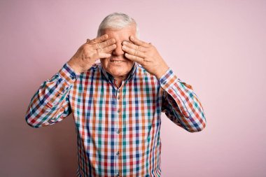 Üst düzey yakışıklı beyaz adam, izole edilmiş pembe arka plan üzerine gündelik bir tişört giyiyor. Gözleri kaplıyor ve neşeli ve komik gülümsüyor. Kör kavram.