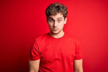 Sarışın, kıvırcık saçlı, kırmızı arka planda sıradan tişörtler giyen, kuşkucu ve gergin, sorun yüzünden üzgün olan genç bir adam. Negatif kişi.