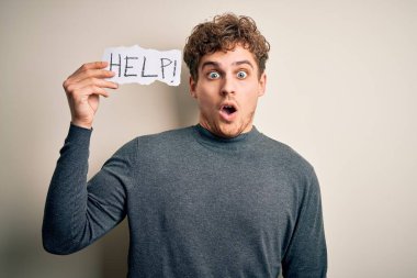 Beyaz arka planda yardım mesajı taşıyan kıvırcık saçlı genç bir adam. Şaşırmış bir yüzle korkmuş ve korku ifadesinden heyecanlanmış.