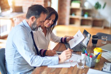 Mutlu ve kendinden emin gülümseyen iki orta yaşlı iş adamı. Ofiste dizüstü bilgisayarla gülümseyerek birlikte çalışıyoruz.