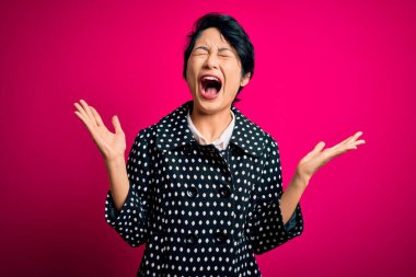 Genç, güzel Asyalı bir kız. Sıradan bir ceket giymiş. Soyutlanmış pembe arka planda duruyor. Kazanan konsept