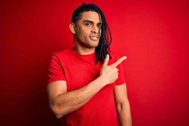 Genç, Afro-Amerikan Afrikalı, rastalı, kırmızı tişörtlü, el parmaklarıyla yüzünü gösteren, ciddi ve sakin bir yüz ifadesi olan bir adam.