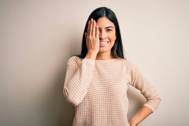 Soyutlanmış arka planda zarif pembe süveter giyen genç, güzel İspanyol bir kadın bir gözünü elinle kapatıyor, yüzünde kendine güvenen bir gülümseme ve sürpriz bir duygu var..