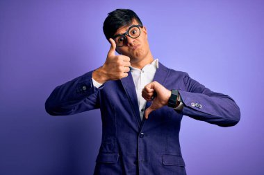 Ceket ve gözlük takan yakışıklı genç bir iş adamı mor arka planda baş parmak kaldırıyor, anlaşmazlık ve anlaşma ifadesi sergiliyor. Çılgın çatışma