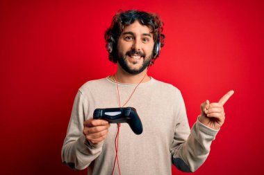 Kıvırcık saçlı ve sakallı genç oyuncu oyun oynuyor, joystick ve kulaklık kullanıyor.