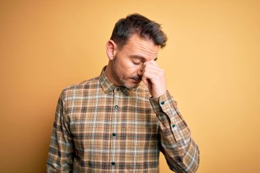 İzole edilmiş sarı arka planda dikilen sıradan tişört giyen genç yakışıklı yorgun burnu ve gözleri ovuşturarak yorgunluk ve baş ağrısı hissediyordu. Stres ve hüsran kavramı.