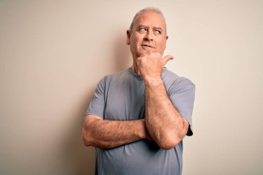 Orta yaşlı yakışıklı, beyaz tişörtlü, izole edilmiş beyaz arka planda duran mutlu yüzüyle gülümseyen ve baş parmağıyla yan tarafı gösteren beyaz bir adam..