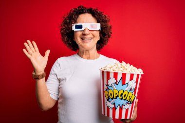 Orta yaşlı kıvırcık saçlı kadın 3 boyutlu gözlük takıp film izliyor. Patlamış mısır yiyor. Çok mutlu ve heyecanlı.