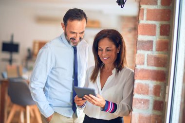 Mutlu ve kendinden emin gülümseyen iki orta yaşlı iş adamı. Ofiste tablet kullanarak birlikte çalışmak, gülümsemek.