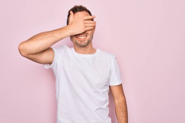 Mavi gözlü yakışıklı bir adam pembe arka planda dikilmiş sıradan beyaz tişörtler giyiyor. Gülümsüyor ve elleri yüzünde şaşkınlıktan gözleri kapatıyordu. Kör kavram.