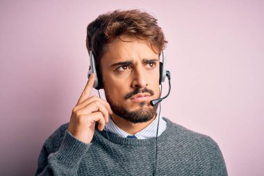 Sakallı, pembe kulaklık takan genç bir çağrı merkezi ajanı. Elleri çenesinde soru sorarken, düşünceli bir ifade takınıyor. Düşünceli bir yüzle gülümsüyor. Şüphe kavramı.