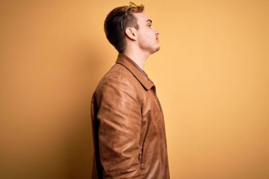 Genç, kızıl saçlı, günlük deri ceket giyen izole edilmiş sarı arka planda rahat bir görünüm ve kendine güvenen bir gülümseme takınan yakışıklı bir adam..