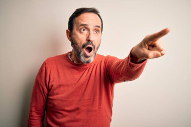 Orta yaşlı, turuncu süveter giyen, izole edilmiş beyaz arka plan üzerinde duran, parmağı önde olan, ağzı açık, ağzı açık, şaşırmış bir adam.