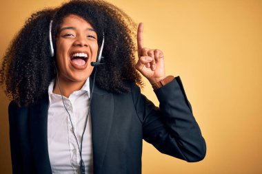 Afro saçlı, sarı arka planda kulaklık takan Afro-Amerikan genç bayan başarılı bir fikir işaret ediyor. Heyecanlı ve mutlu. Bir numara..
