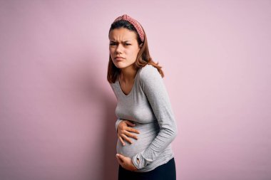 Genç, güzel bir kız hamile, pembe arka planda, midesi ağrıyan, hazımsızlık çeken ve kendini kötü hisseden bir bebek bekliyor. Ache kavramı.
