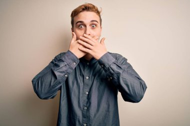 İzole edilmiş beyaz arka planda dikilen gündelik tişört giyen genç, kızıl saçlı adam yanlışlıkla ağızlarını kapatarak şok geçirdi. Gizli konsept.