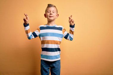 Sarı arka plan üzerinde mavi çizgili gömlek giyen, umut ve gözlerin kapalı bir şekilde gülümseyen küçük beyaz çocuk. Şans ve batıl inanç..