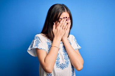 Genç, güzel, esmer bir kadın. Günlük tişört giyiyor. Mavi arka planda duruyor. Depresyon kavramı.