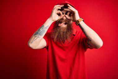 Gözlüklü yakışıklı teslimatçı ve izole edilmiş arka planda kırmızı şapkalı. Dürbün gibi güzel hareketler yapıyor. Dürbün dilini çıkarıyor, gözler parmaklarından bakıyor. Çılgın ifade.