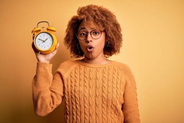 Kıvırcık saçlı, eskimiş çalar saati olan genç, Afro-Amerikan bir kadın. Şaşırmış bir yüzle korkmuş ve korku ifadesinden heyecanlanmış.