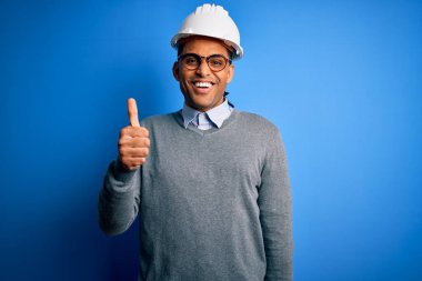 Siyah saçlı, güvenlik kaskı takan, mutlu bir el hareketi yapan Afro-Amerikan mühendis. Kameraya bakıp başarıyı gösteren ifade onaylanıyor.