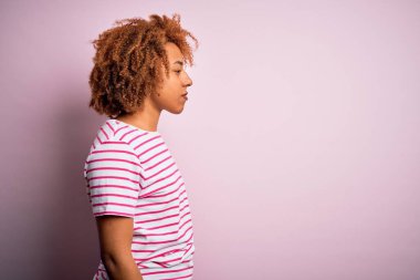 Kıvırcık saçlı, sıradan çizgili tişört giyen, rahat profil pozu veren, kendine güvenen gülümseyen güzel Afro-Amerikan kadın..