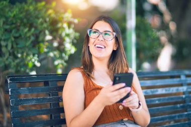 Mutlu ve kendinden emin gülümseyen genç ve güzel bir kadın. Yüzünde gülümsemeyle şehirde akıllı telefon kullanarak oturmak.