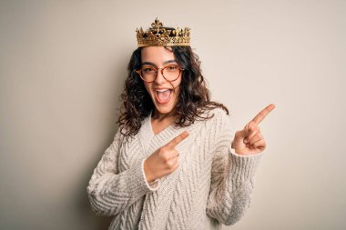 Kıvırcık saçlı, beyaz arka planda altın kraliçenin tacını takan, gülümseyen ve kameraya bakan iki eli ve parmakları kenarda olan güzel bir kadın..