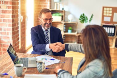 Mutlu ve kendinden emin gülümseyen iki orta yaşlı iş adamı. Birlikte çalışırken gülümseyerek ofiste el sıkışırken.