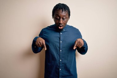 Beyaz arka plan üzerinde duran, reklamını gösteren parmaklarıyla işaret eden, şaşırmış yüz ve ağzı açık genç, Afro-Amerikan bir adam.